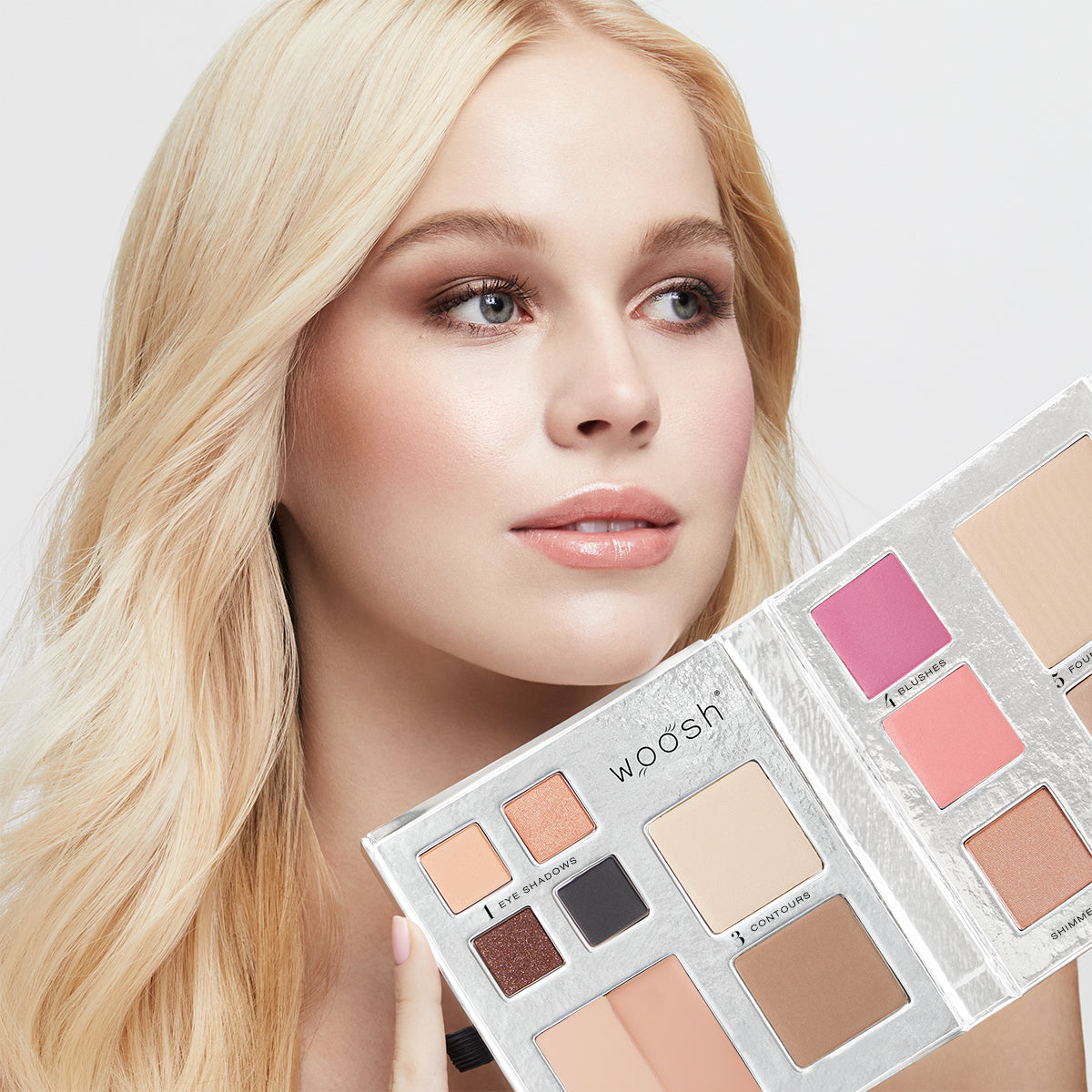 Blonde Model holding the 13 pan Fold out Face palette that includes Eyeshadow, cream concealer, contour, blush, highlight, and foundation powders.