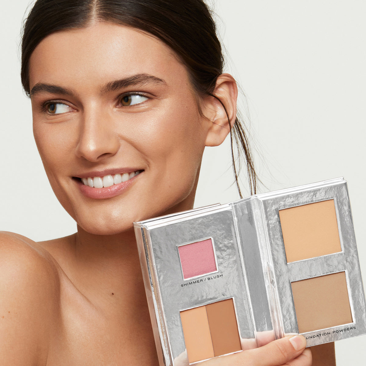 a brunette, tan model with perfect, natural-looking skin holding Fold Out Complexion in shade #2.5 medium tan