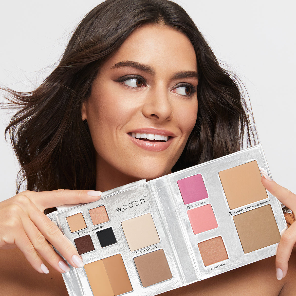 Brunette Model holding the 13 pan Fold out Face palette that includes Eyeshadow, cream concealer, contour, blush, highlight, and foundation powders.