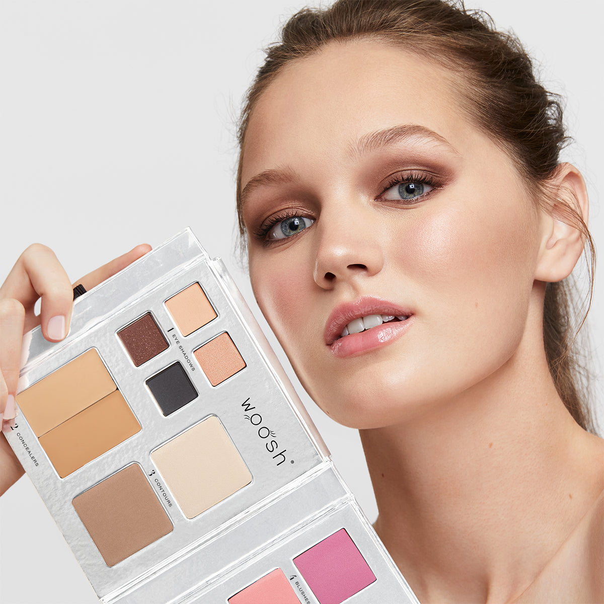 Brunette model holding the 13 pan Fold out Face palette that includes Eyeshadow, cream concealer, contour, blush, highlight, and foundation powders.