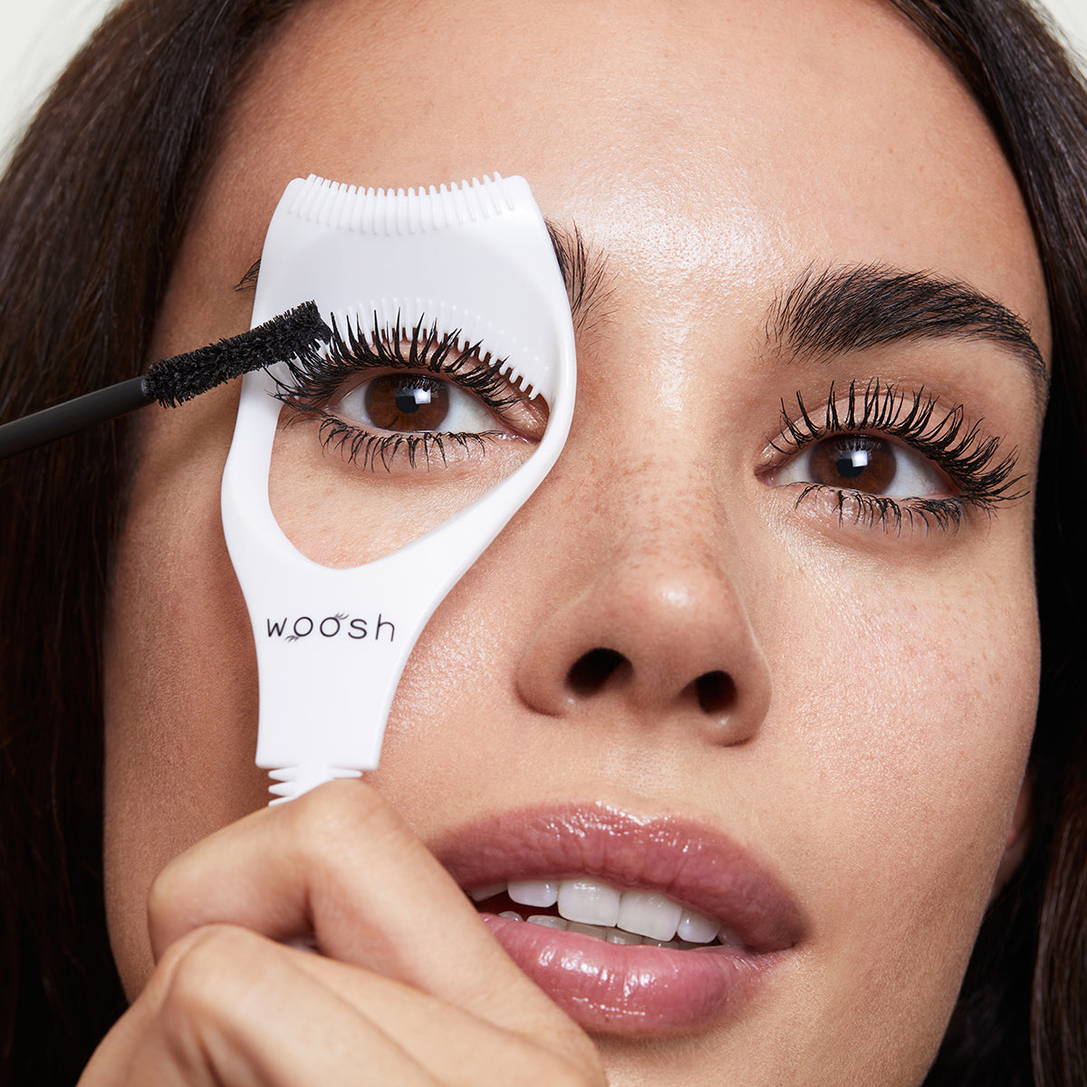 Model using mascara shield on upper lashes as she applies mascara. The shield protects her eyelids from mascara.