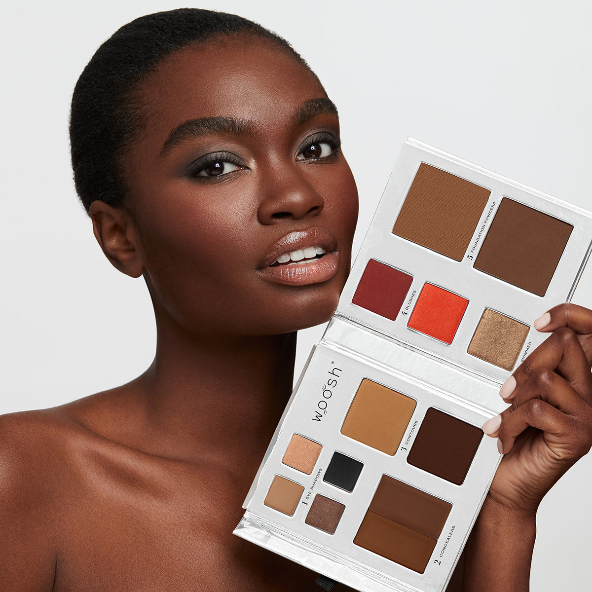 Brunette Model holding the 13 pan Fold out Face palette that includes Eyeshadow, cream concealer, contour, blush, highlight, and foundation powders.