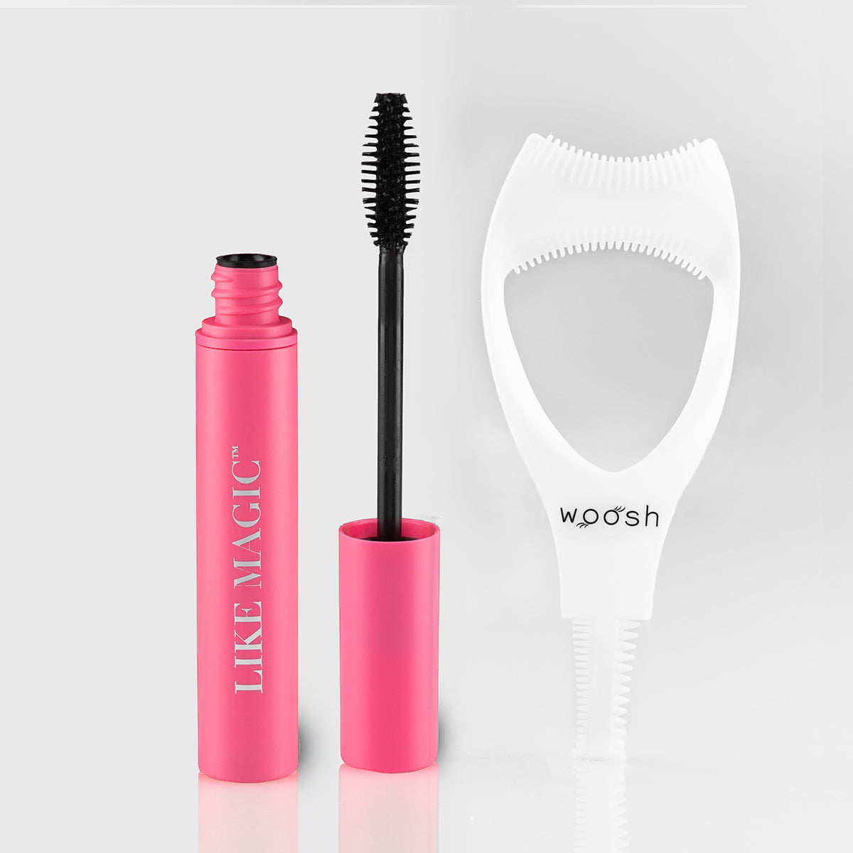Open pink tube of Like Magic mascara showing almond shaped wand and bristles, next to a white mascara shield.