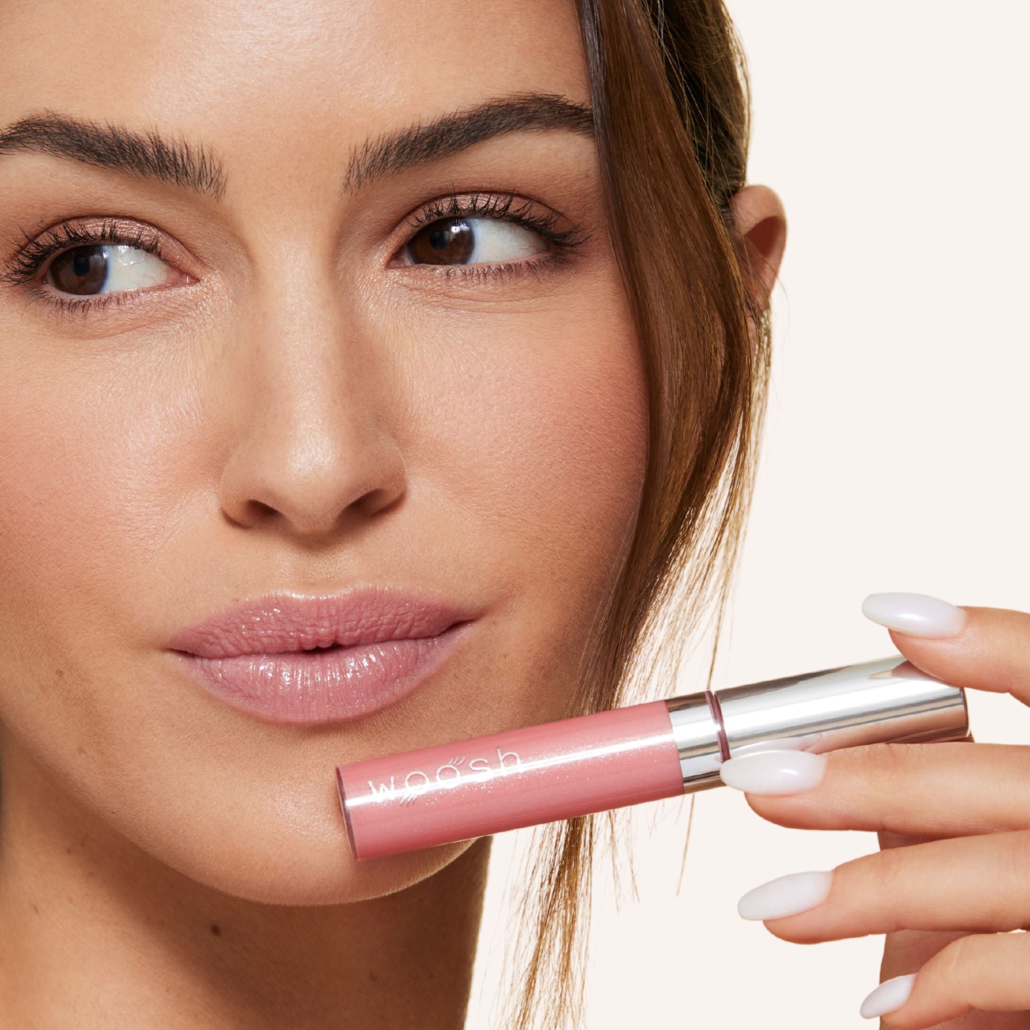 Previously known as glam peach, glimmer is now infused with shea butter and hyaluronic acid. The perfect peach shade with sparkles. Photo of model holding bottle close to lip.