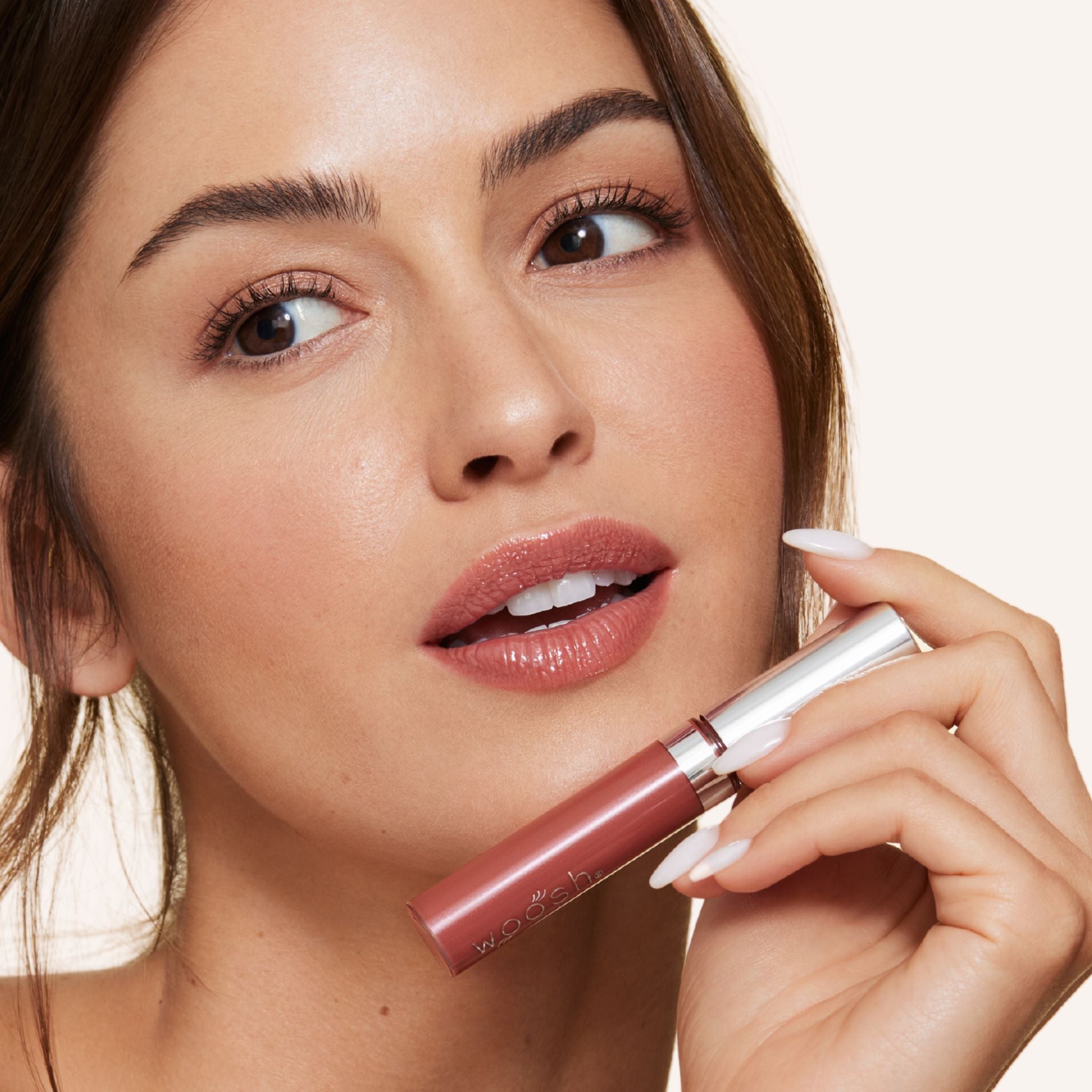 Previously known as Rich Copper, our favorite lip gloss has been renamed to Glow. Now infused with shea butter AND hyaluronic acid. Photo of model holding gorgeous brown nude color to lips