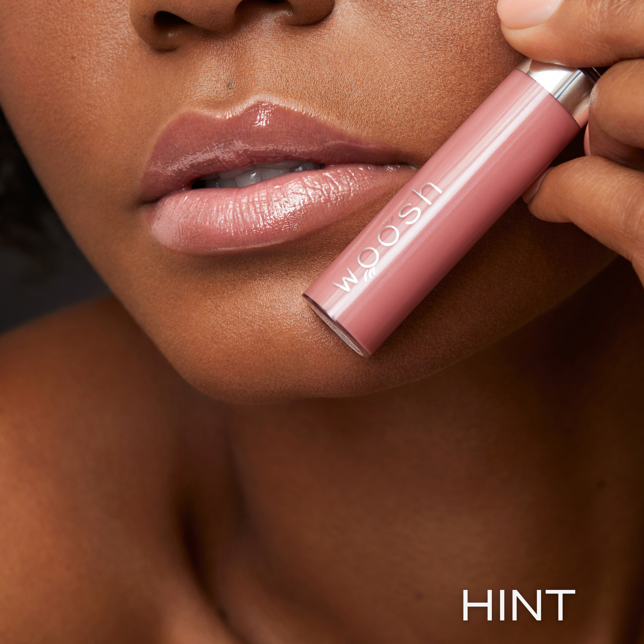 Previously known as beige natural, hint is now infused with shea butter and hyaluronic acid. The perfect nude light pink shade. Photo of model holding bottle close to lip.