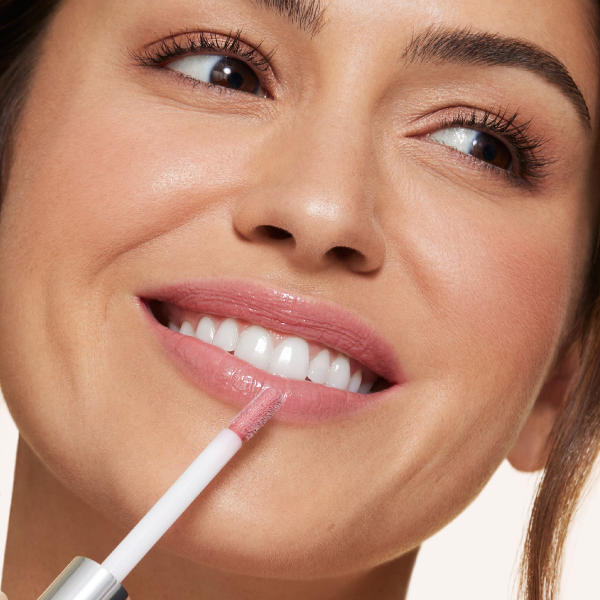 Previously known as beige natural, hint is now infused with shea butter and hyaluronic acid. The perfect nude light pink shade. Photo of model applying gloss to lip