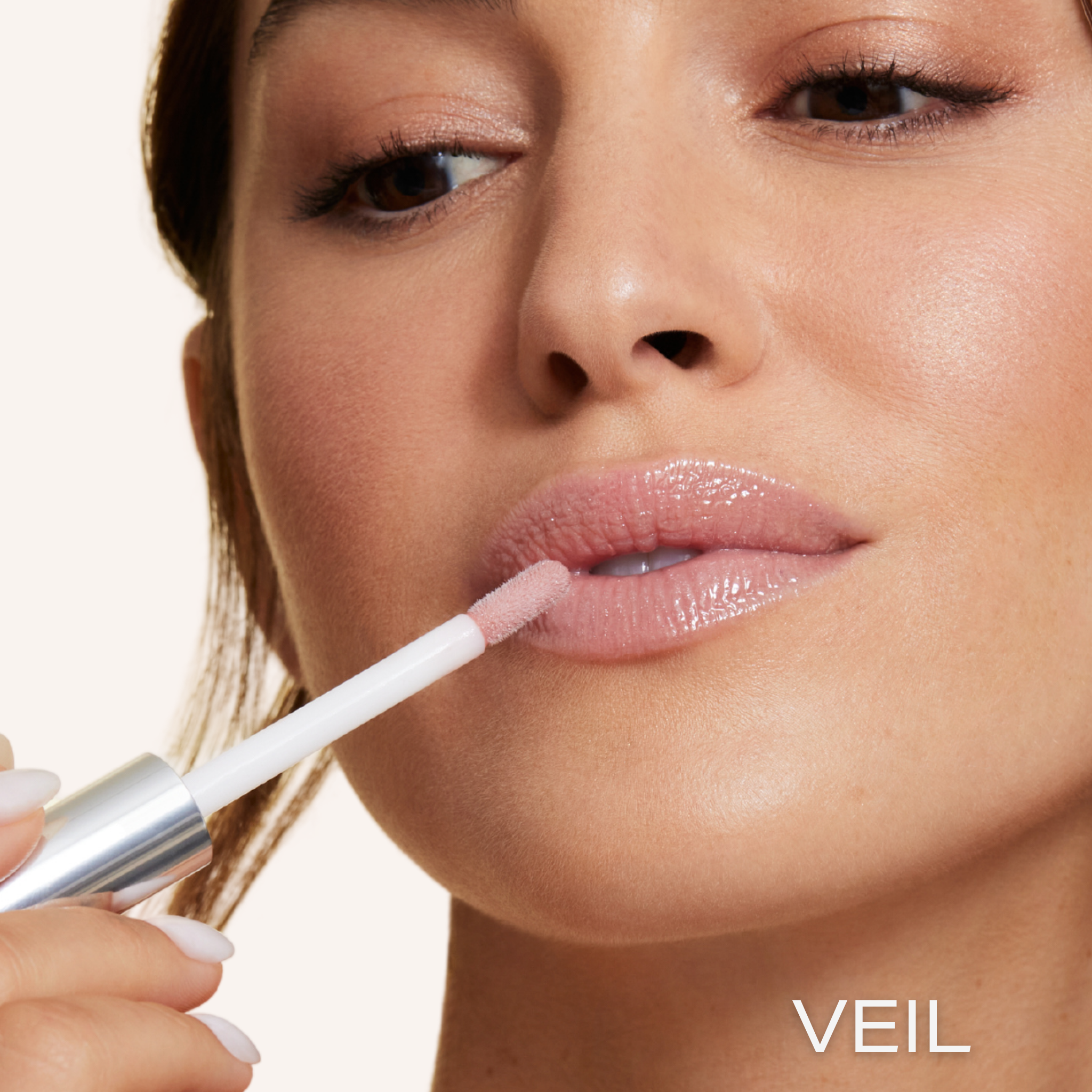 Previously known as beige frosted, our favorite lip gloss has been renamed to veil. Now infused with shea butter AND hyaluronic acid. Photo of model applying gorgeous nude color to lips
