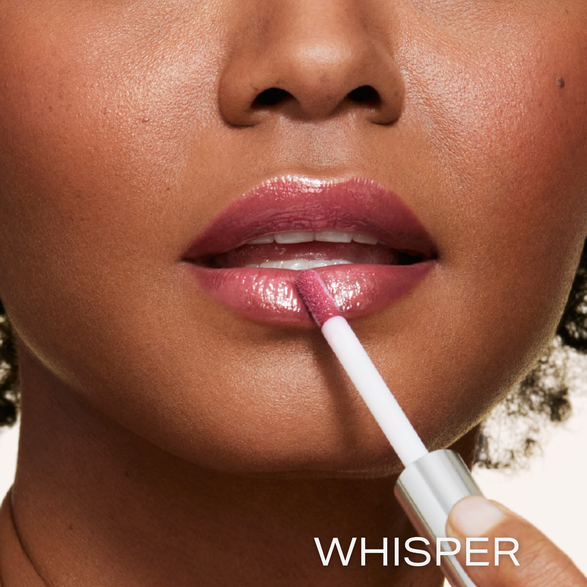 New shade whisper is a purple berry shade infused with shea butter and hyaluronic acid. . closeup shot of model applying gloss on lip