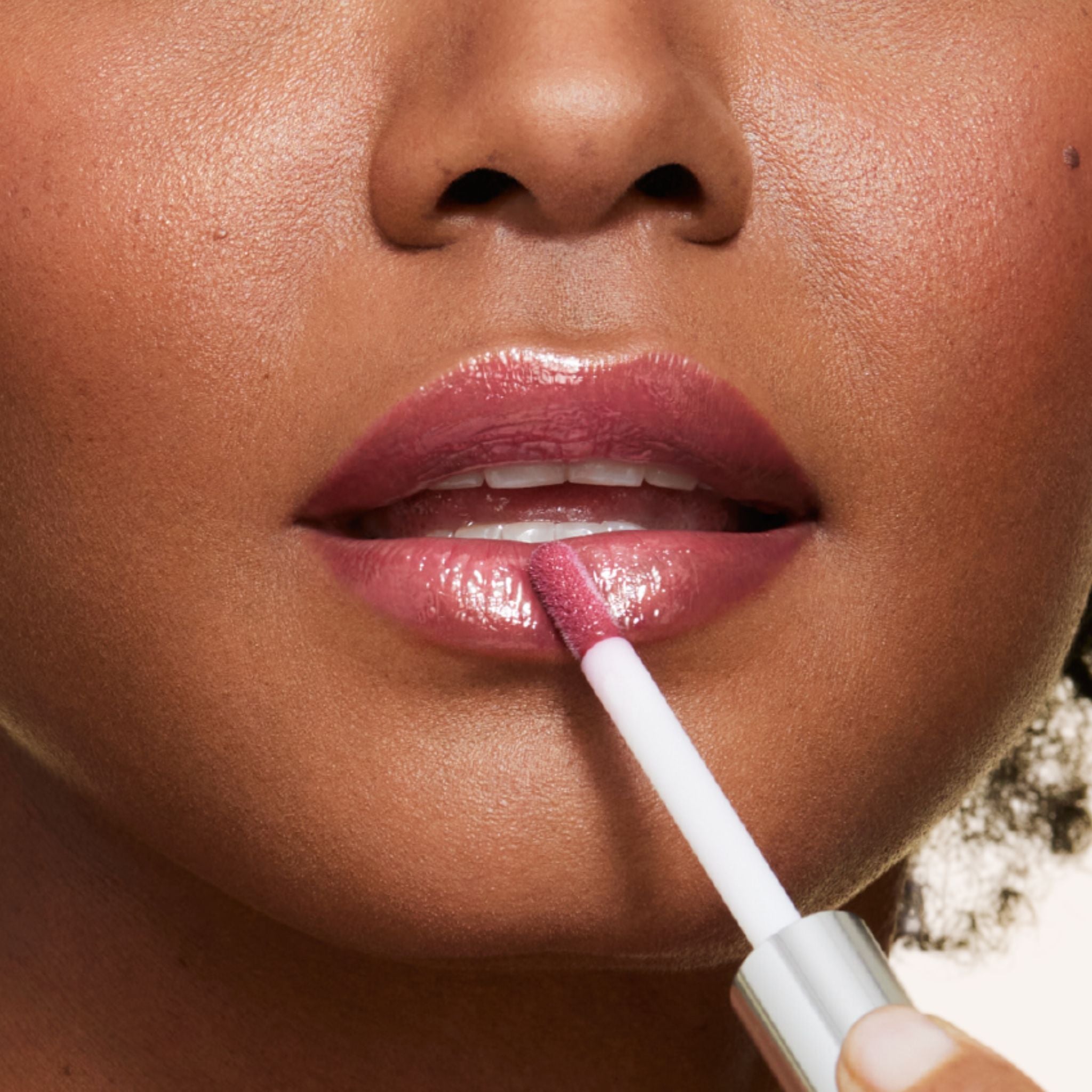 New shade whisper is a purple berry shade infused with shea butter and hyaluronic acid. . closeup shot of model applying gloss on lip