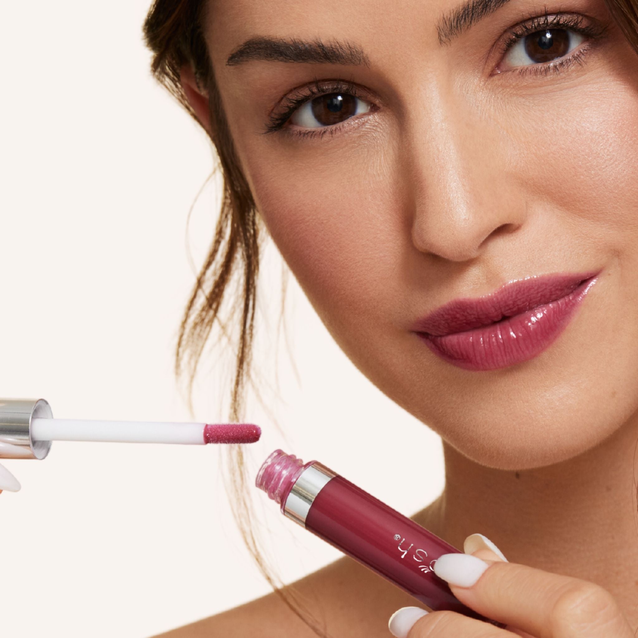 New shade whisper is a purple berry shade infused with shea butter and hyaluronic acid. . closeup shot of model applying gloss on lip