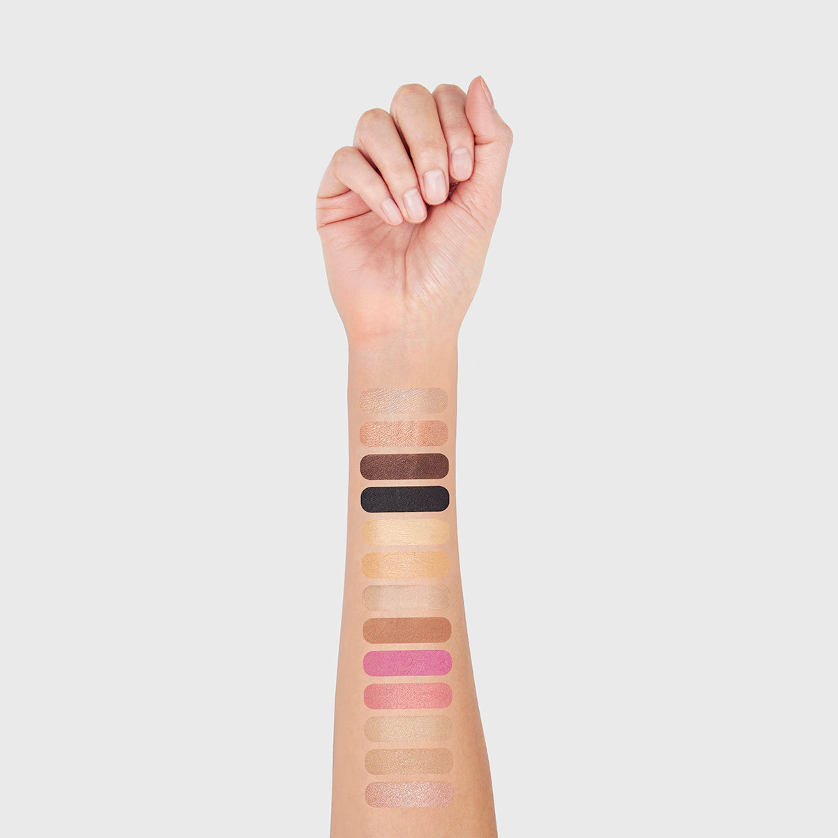 a photo of a light-skinned woman's arm with 13 swatches showing all 13 cosmetics that are found in the fold out face #2 medium light palette