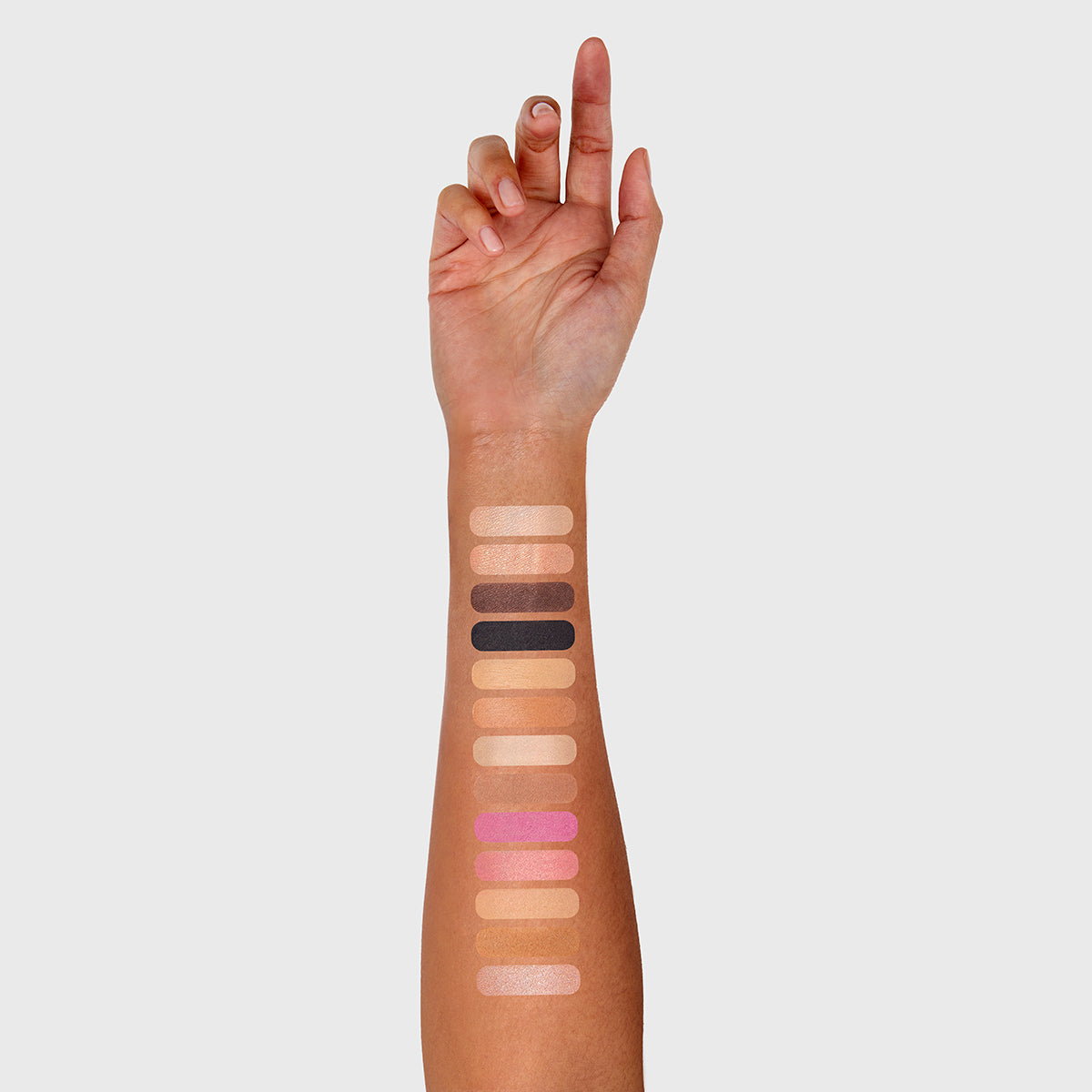 a photo of a tan, multi-ethnic, or hispanic woman's arm with 13 swatches showing all 13 cosmetics that are found in the fold out face #3 medium palette