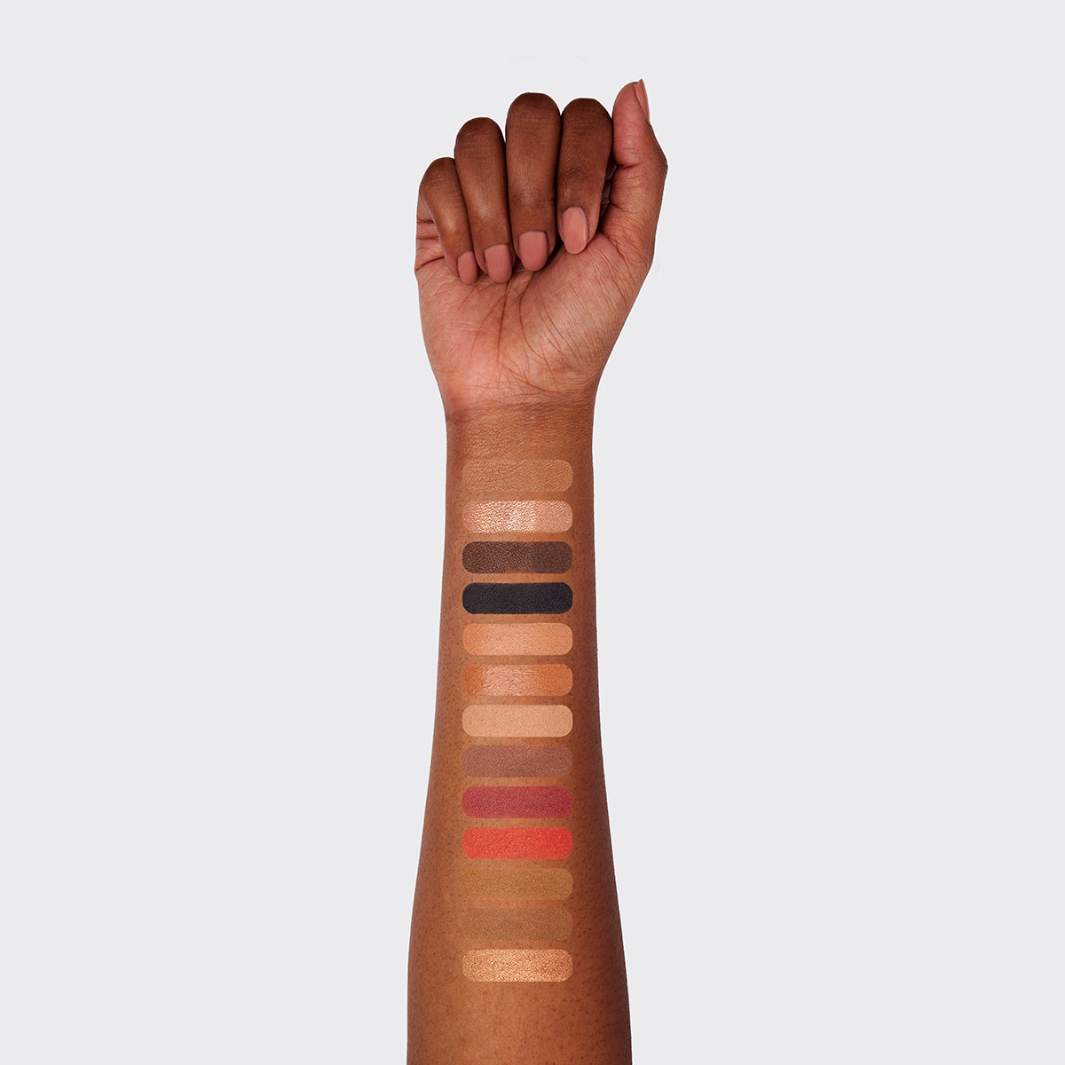 a photo of a dark-skinned woman's arm with 13 swatches showing all 13 cosmetics that are found in the fold out face #4 medium deep palette