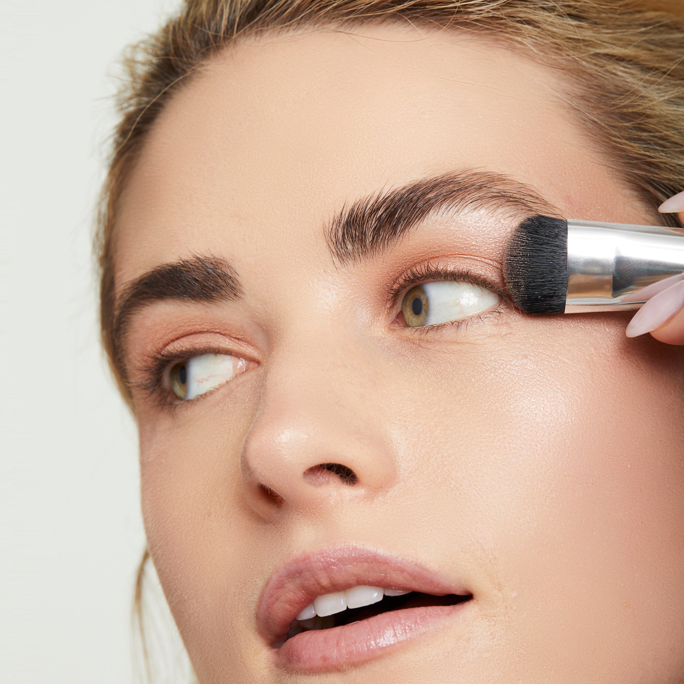Model sweeping eye shadow on lids with the larger end of the Essential Eye Brush