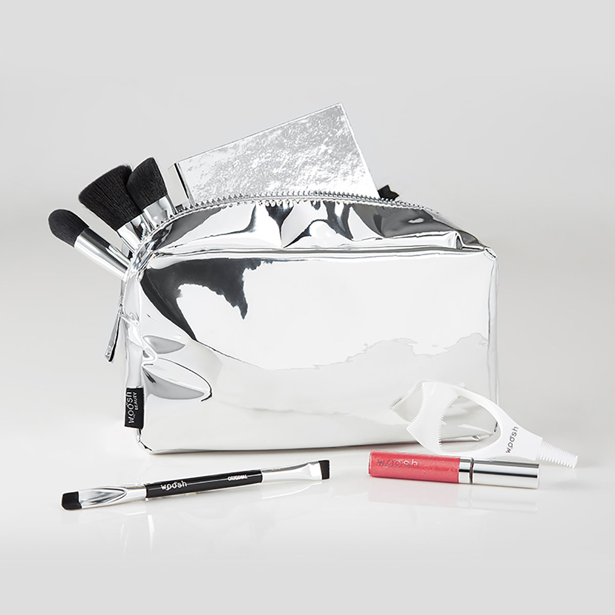 Demonstration of what you can fit in the Woosh Beauty silver essential makeup bag shown with Woosh Beauty essential products