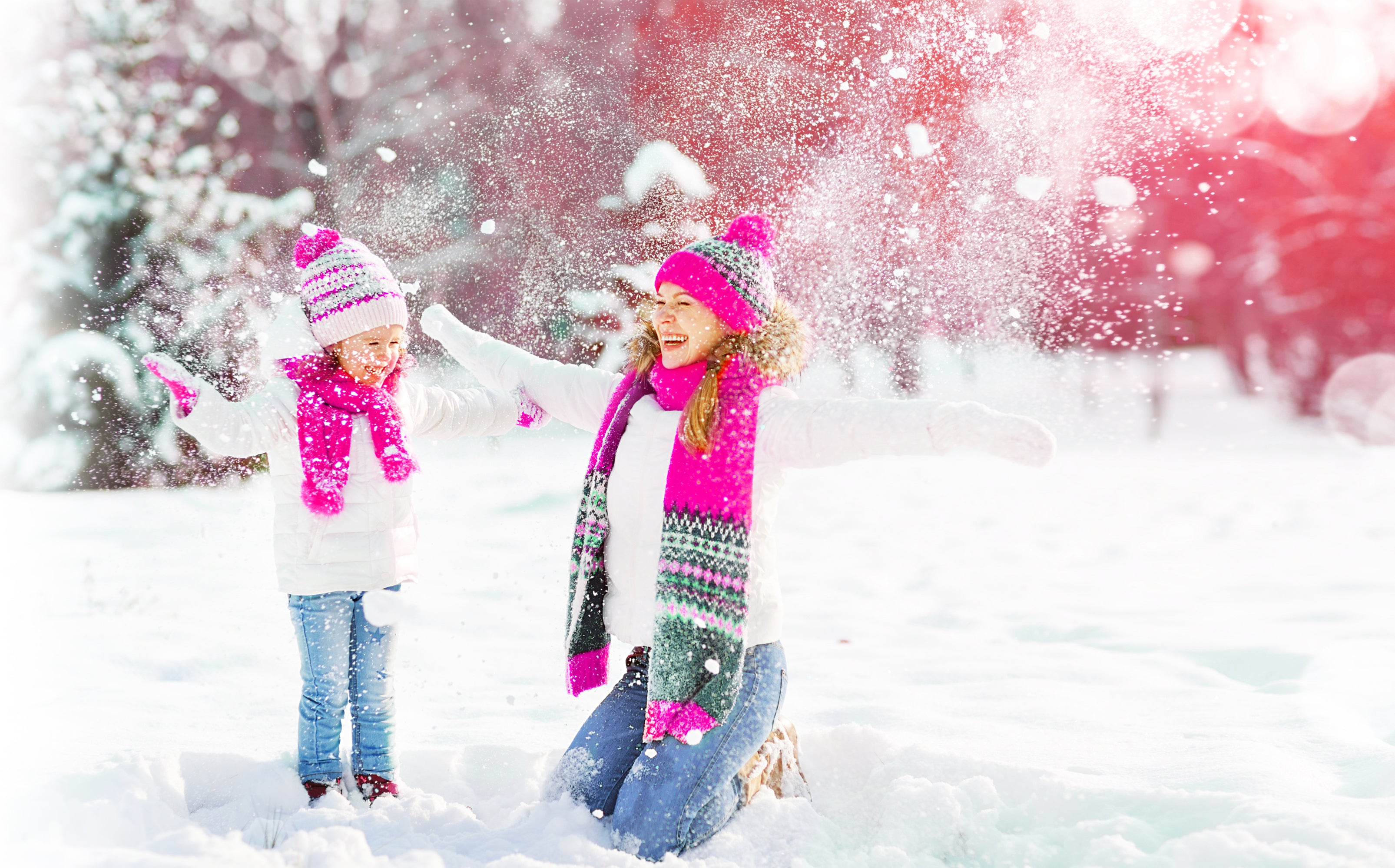 Mother and daughter wearing pink hats and scarfs playing in the snow