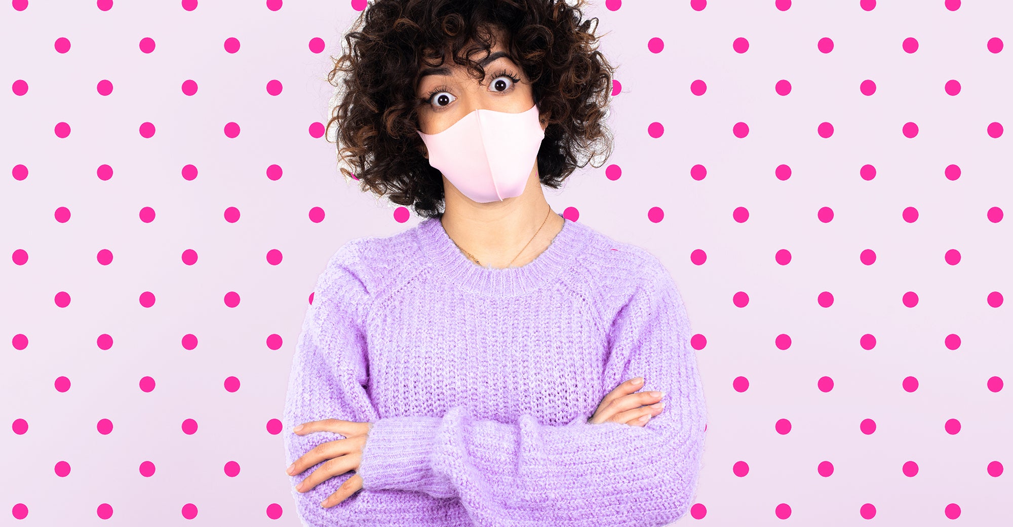 Woman with curly hair wearing a mask in front of a pink background