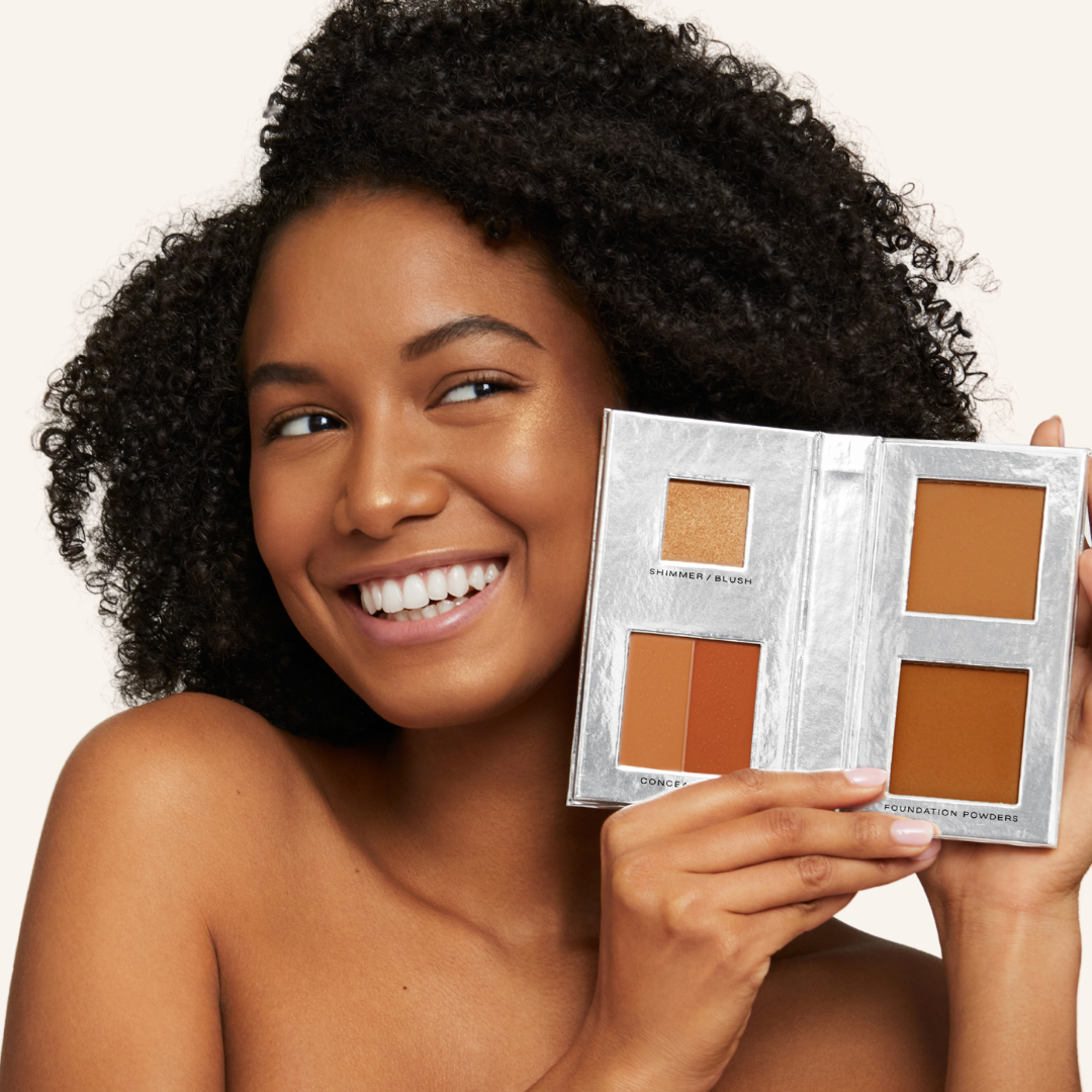 a curly-haired, African American model with perfect, natural-looking skin holding Fold Out Complexion in shade #4 medium deep