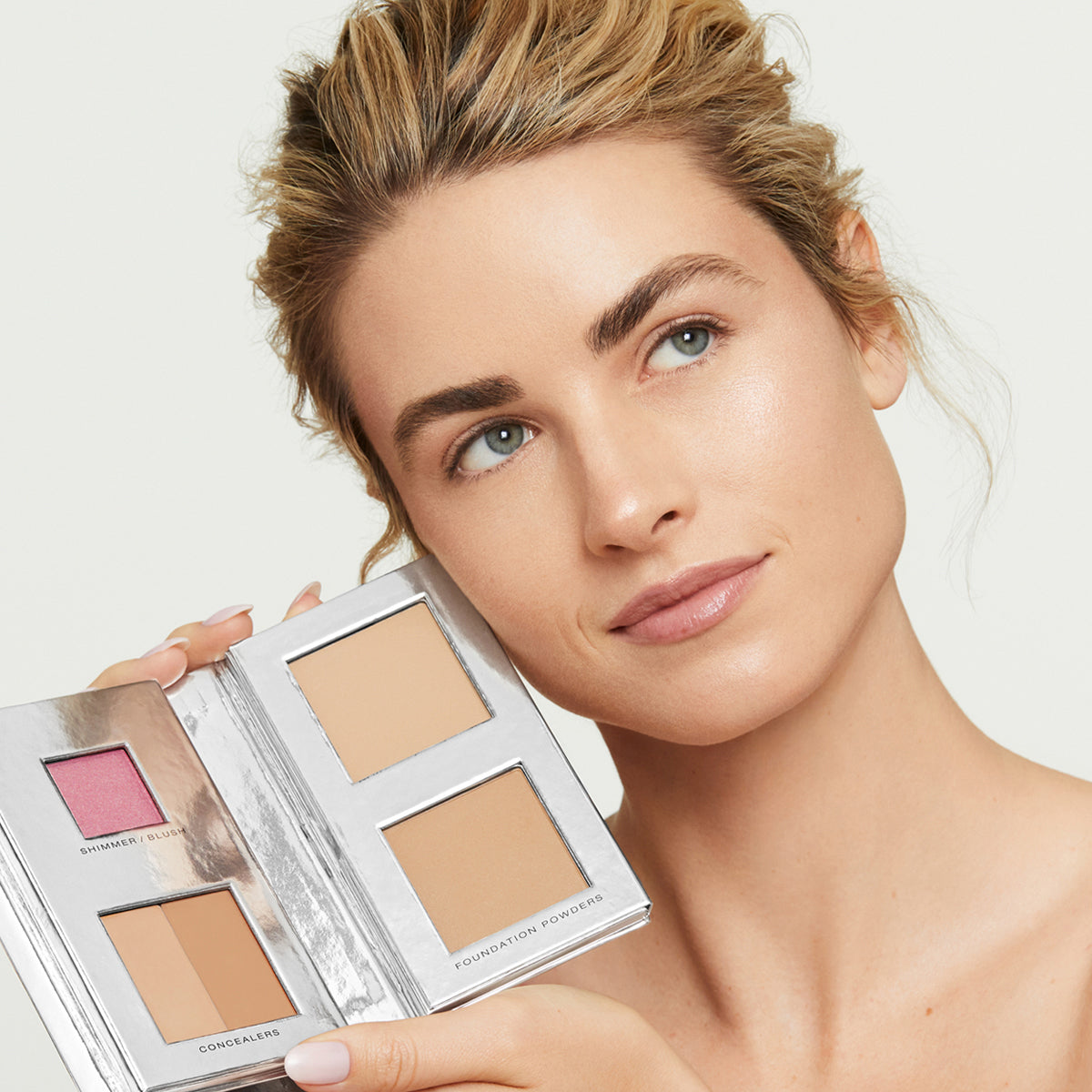 a blonde, light-skinned model with perfect, natural-looking skin holding Fold Out Complexion in shade #2 medium light