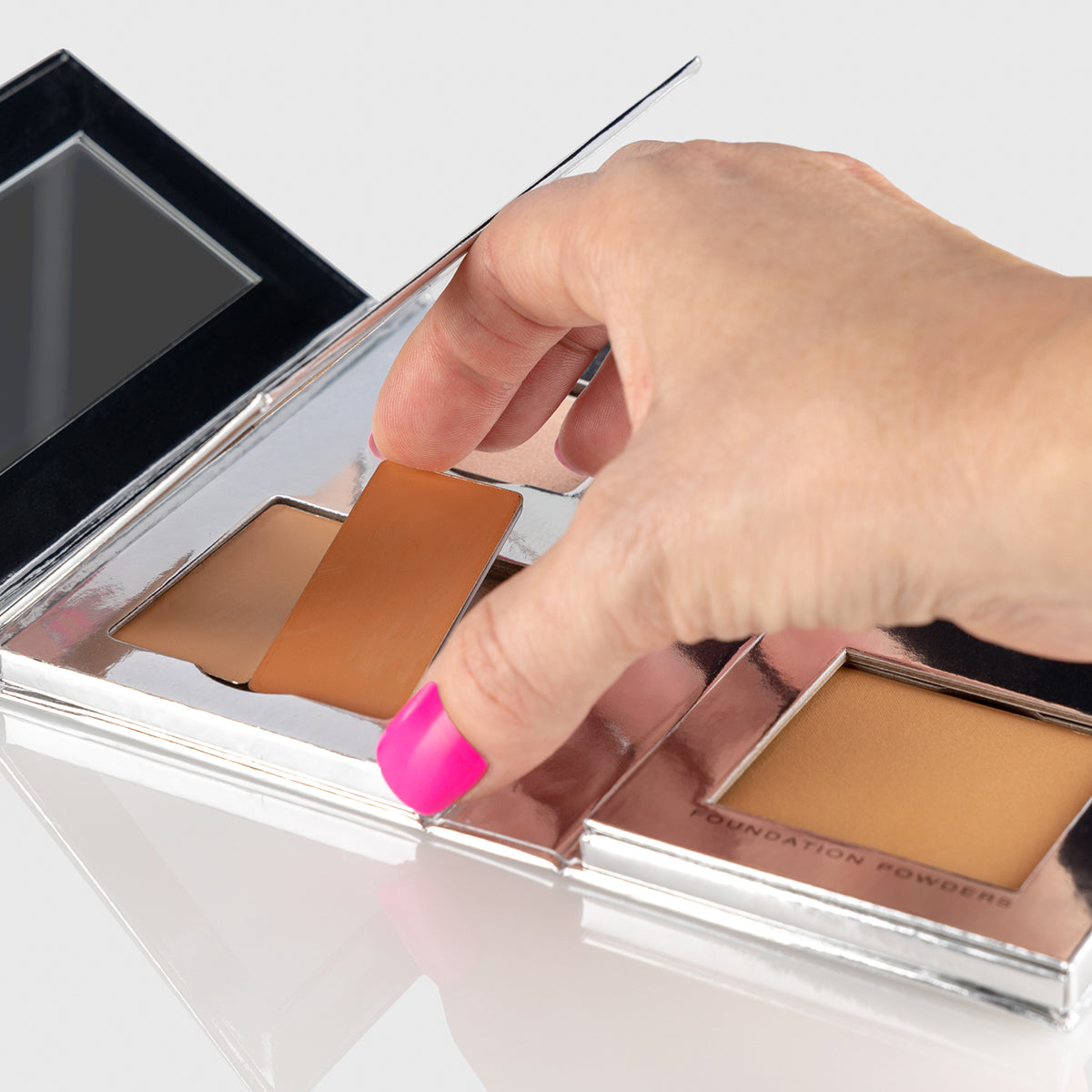a photo of a woman's hand showing how to remove and replace one of the individual pans of makeup in the Fold Out Complexion palette
