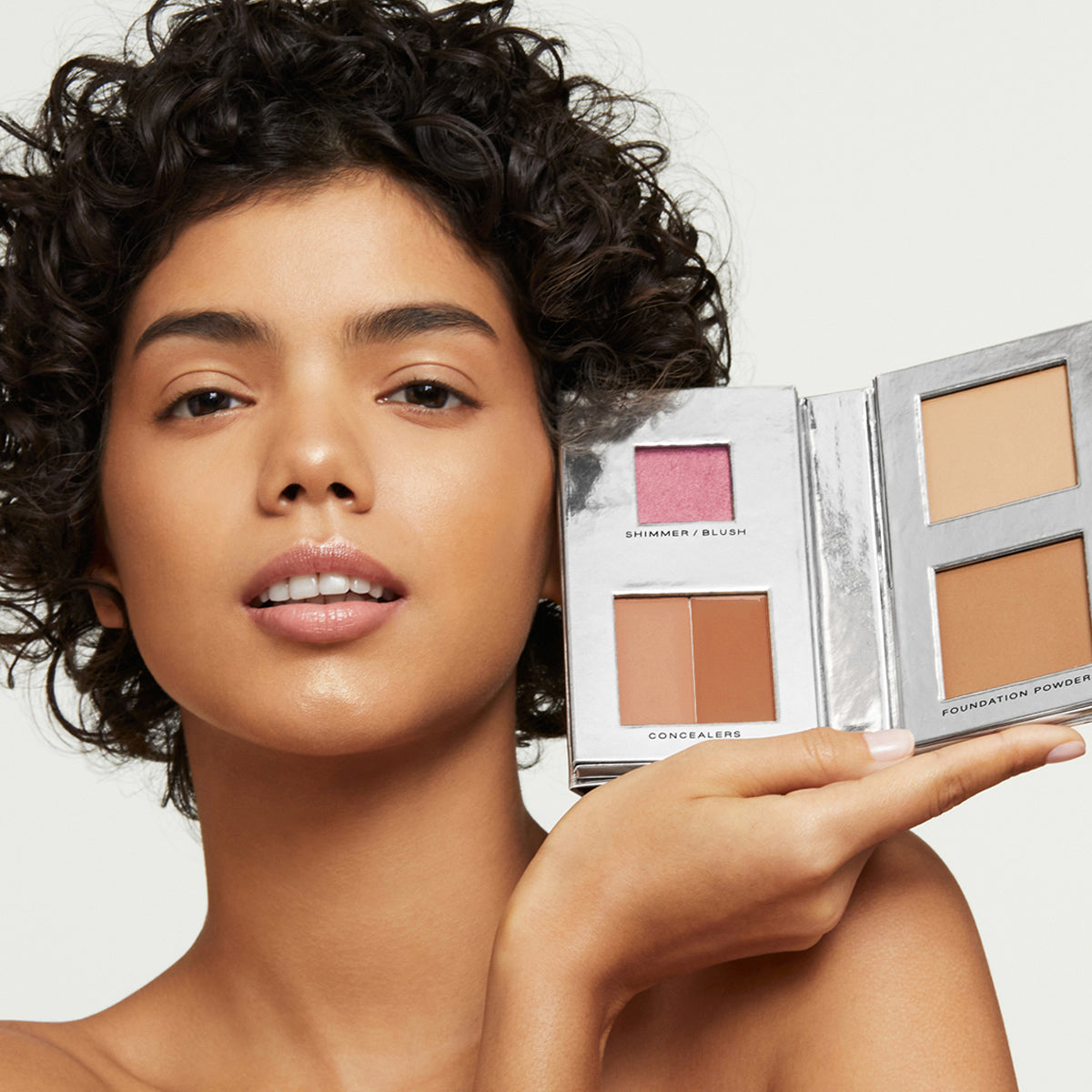 a curly-haired, multi-ethnic model with perfect, natural-looking skin holding Fold Out Complexion in shade #3 medium