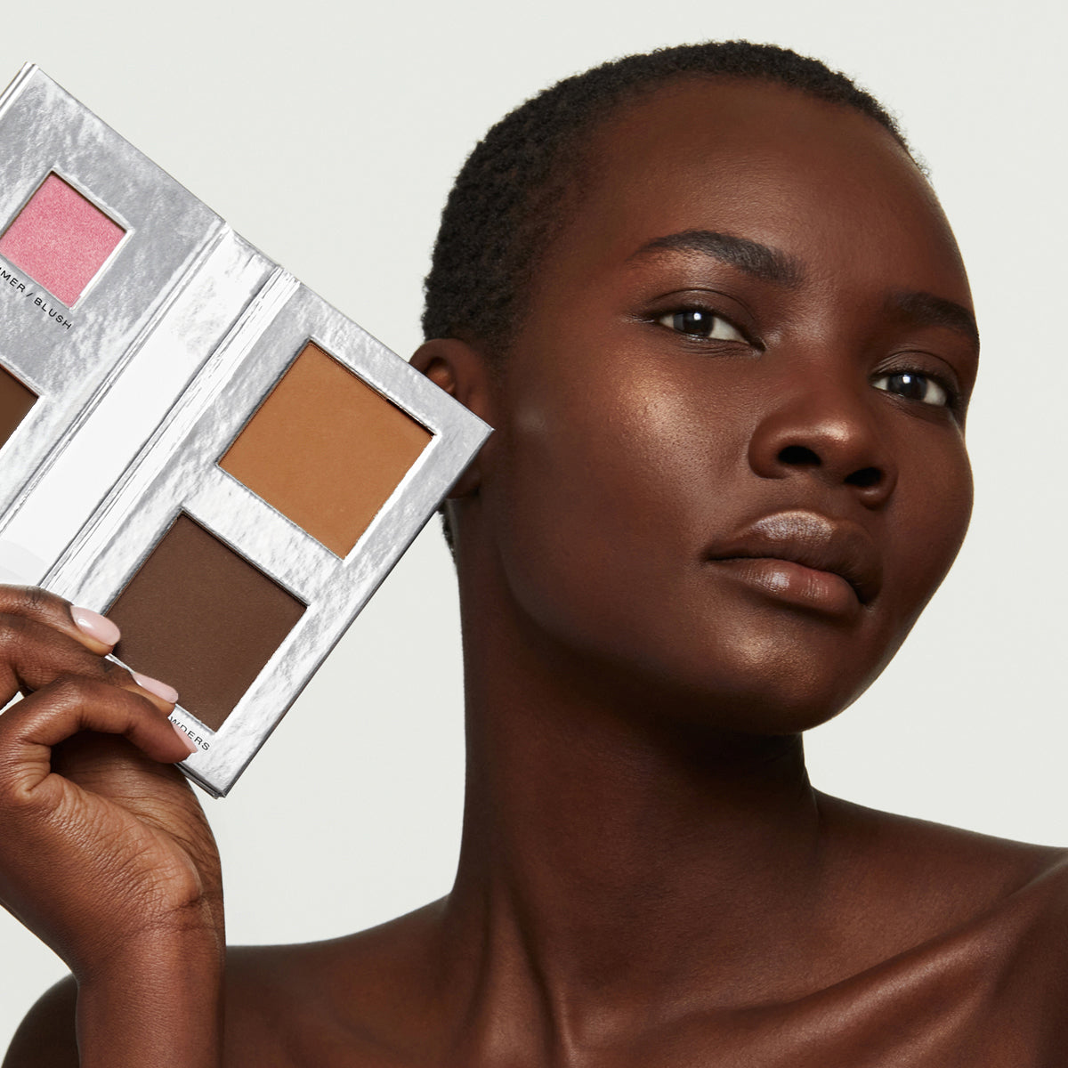 a short-haired, deep toned African model with perfect, natural-looking skin holding Fold Out Complexion in shade #4 medium deep