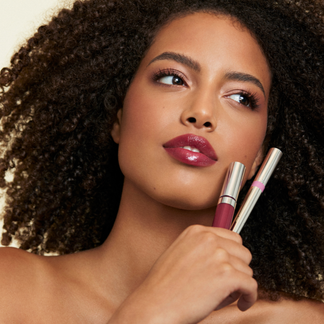 Image of model holding up the duo with spin on gloss in whisper and monogamous stain steadfast. Model has bottles near face with products applied to lip 