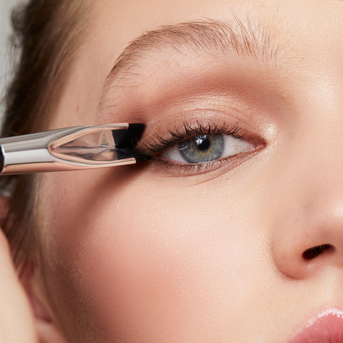 a photo of a pretty woman stamping a v-shaped makeup brush down onto the outer corner of her eye