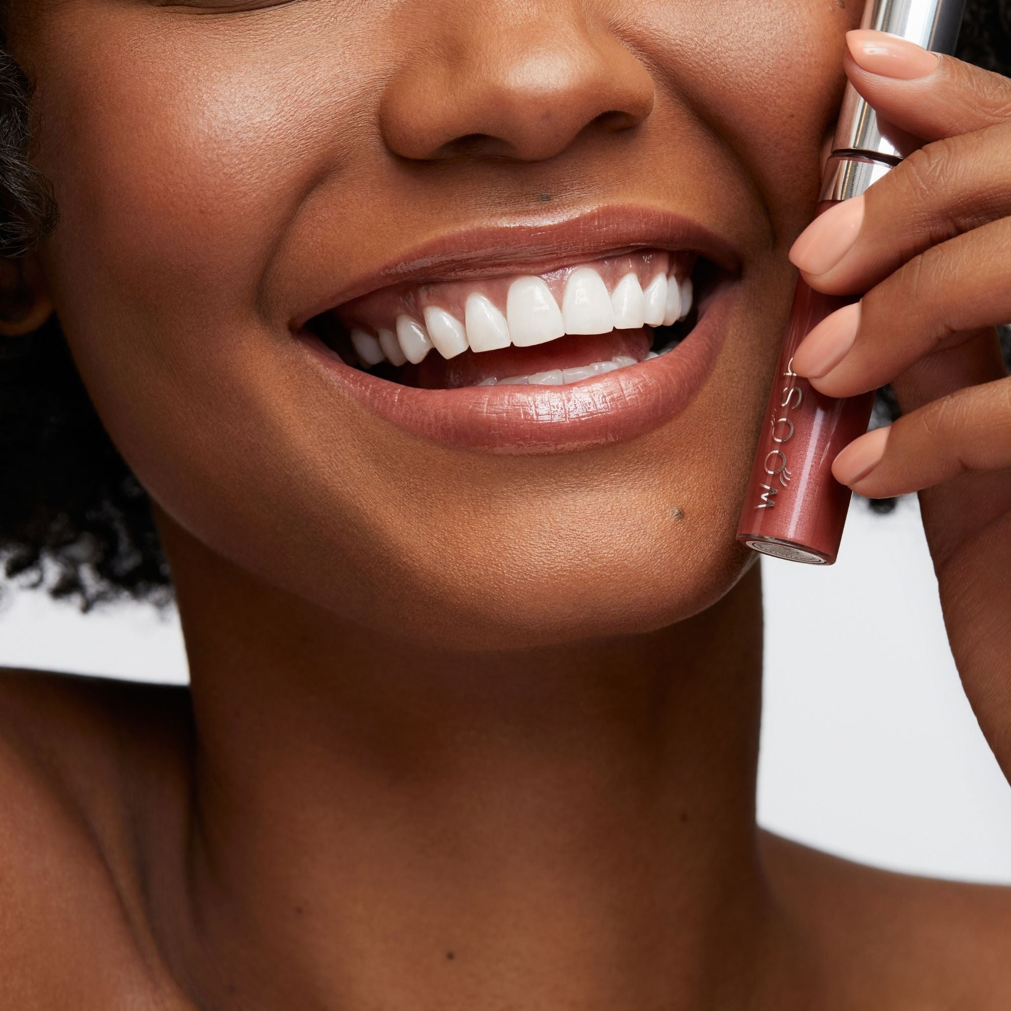 Previously known as Rich Copper, our favorite lip gloss has been renamed to Glow. Now infused with shea butter AND hyaluronic acid. Photo of model holding gorgeous brown nude color to lips