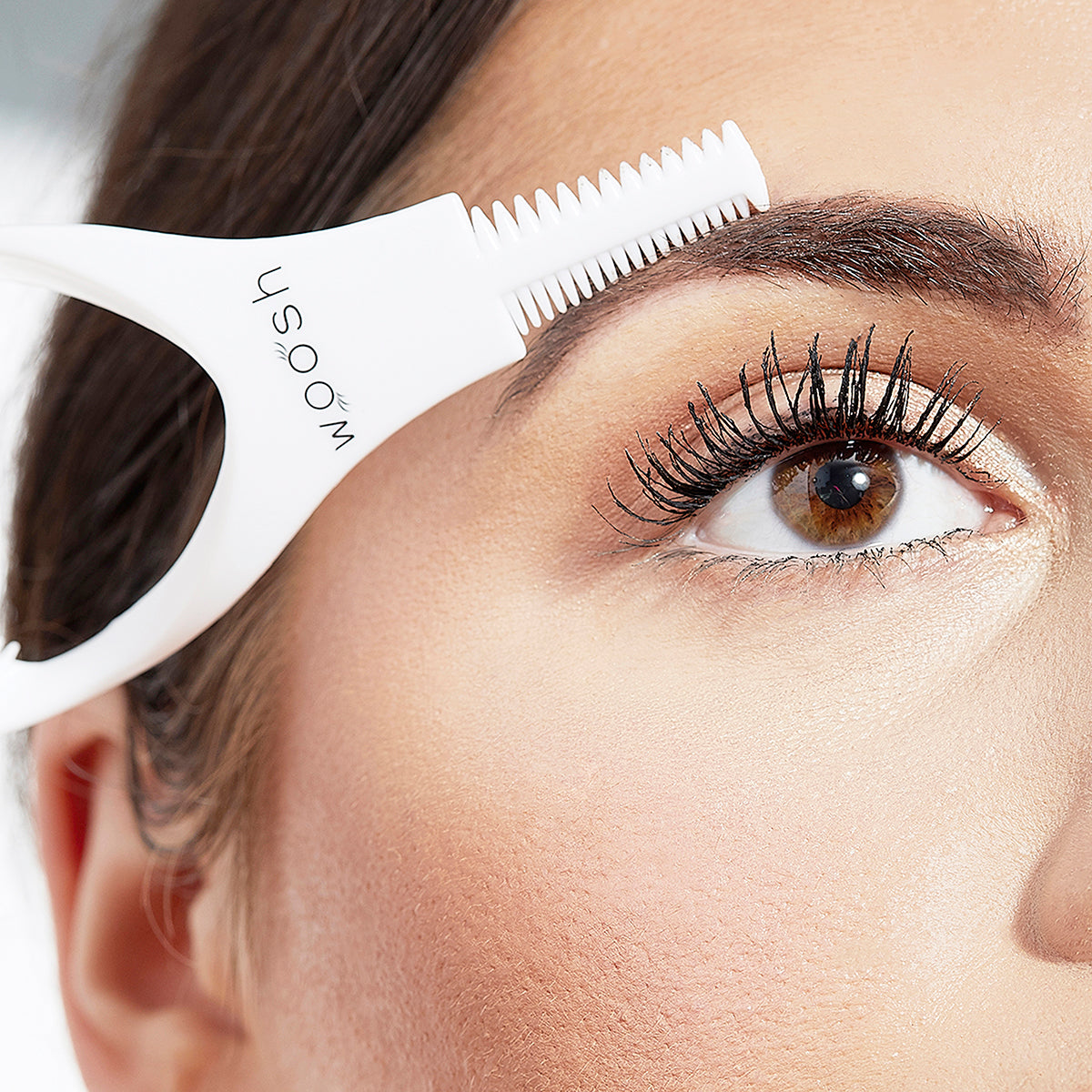 Woman using the handle end of the mascara shield to comb her eyebrows 