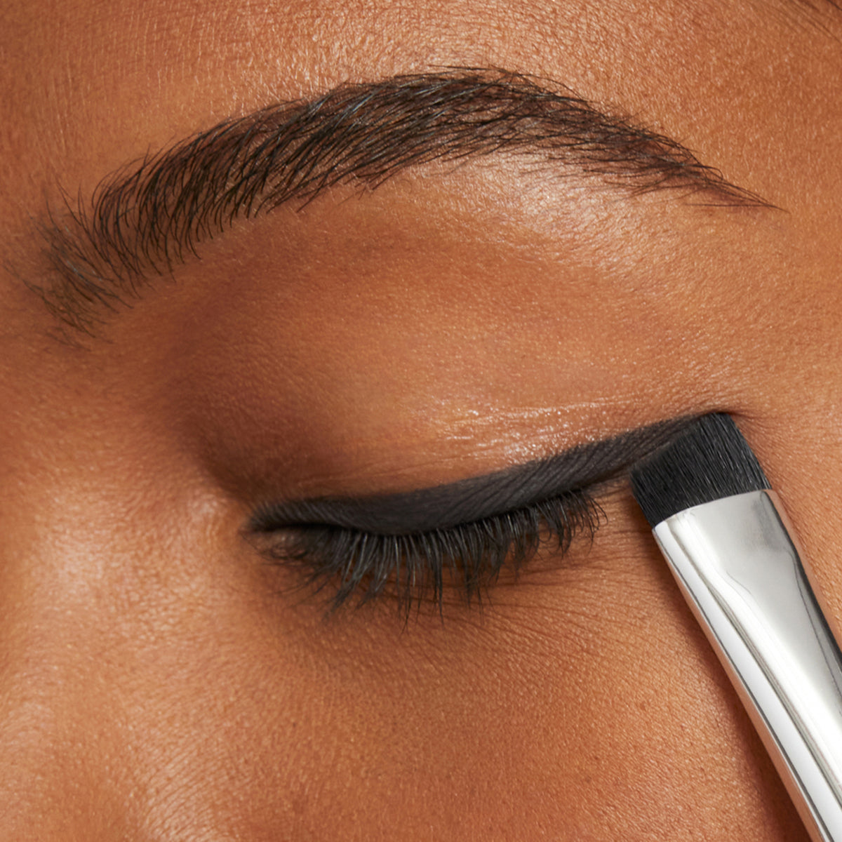 Model applying LIcorice eye shadow as eyeliner