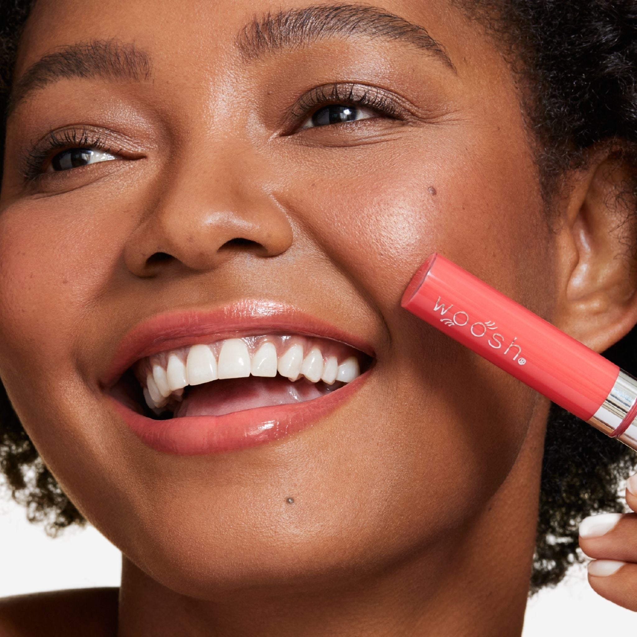 New shade splash is a bright coral shade infused with shea butter and hyaluronic acid. . closeup shot of model holding bottle close to lip 
