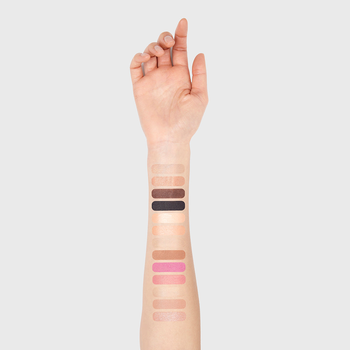 a photo of a light-skinned woman's arm with 13 swatches showing all 13 cosmetics that are found in the fold out face #1 light palette