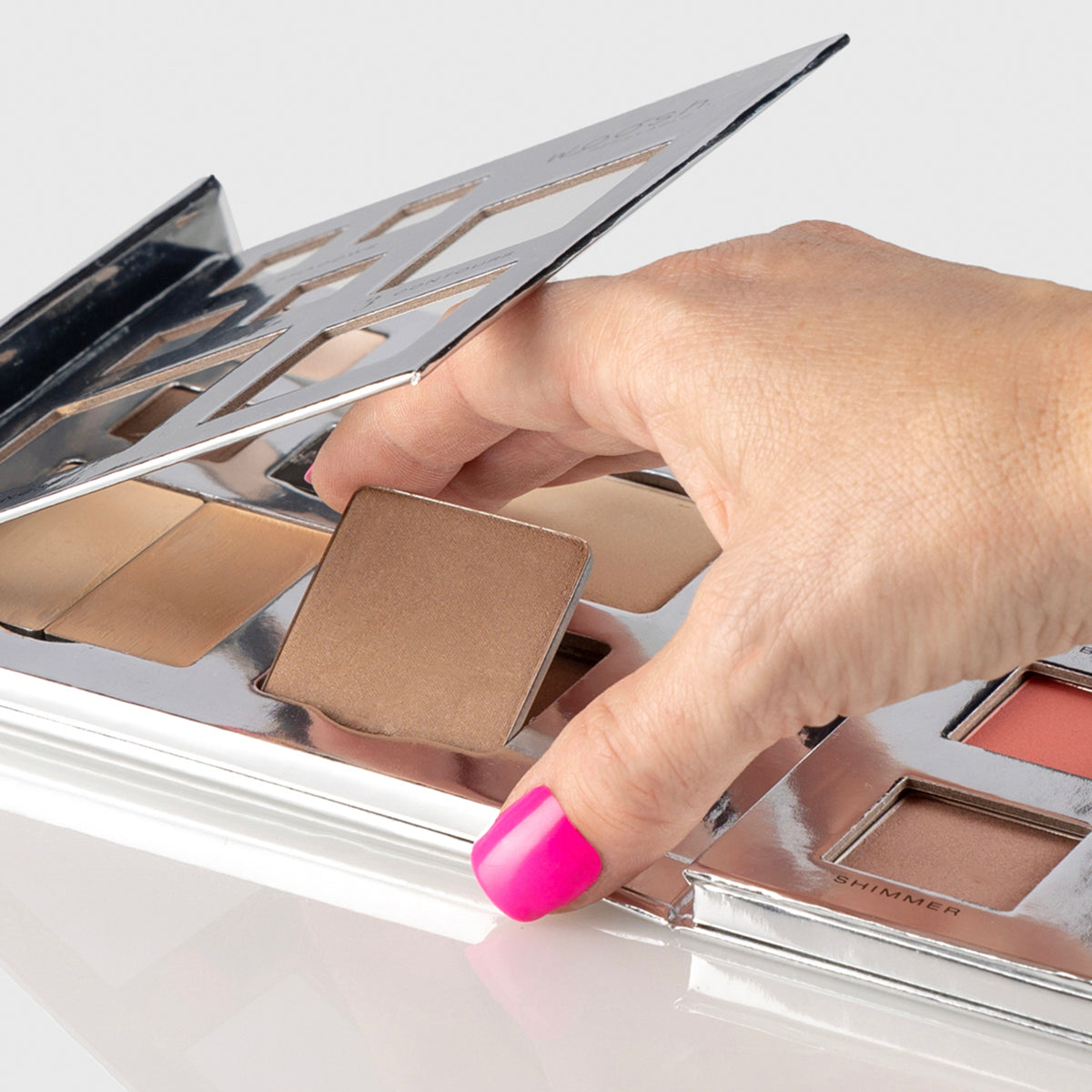 a photo of a silver makeup palette with a woman's hand showing how to remove and replace one of the individual pans of makeup inside