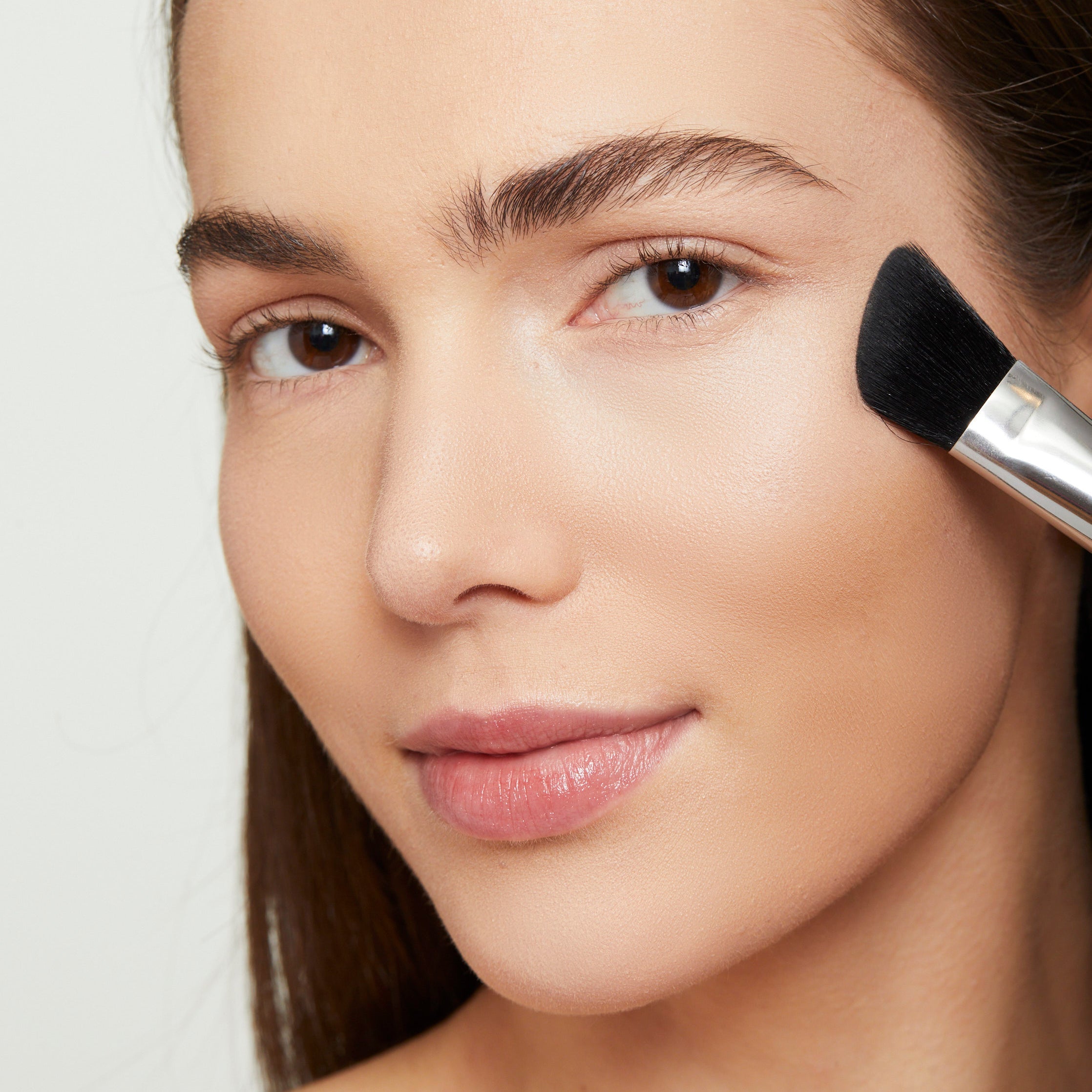 Model applying highlighter to the cheeks with the angled end of the essential contour brush