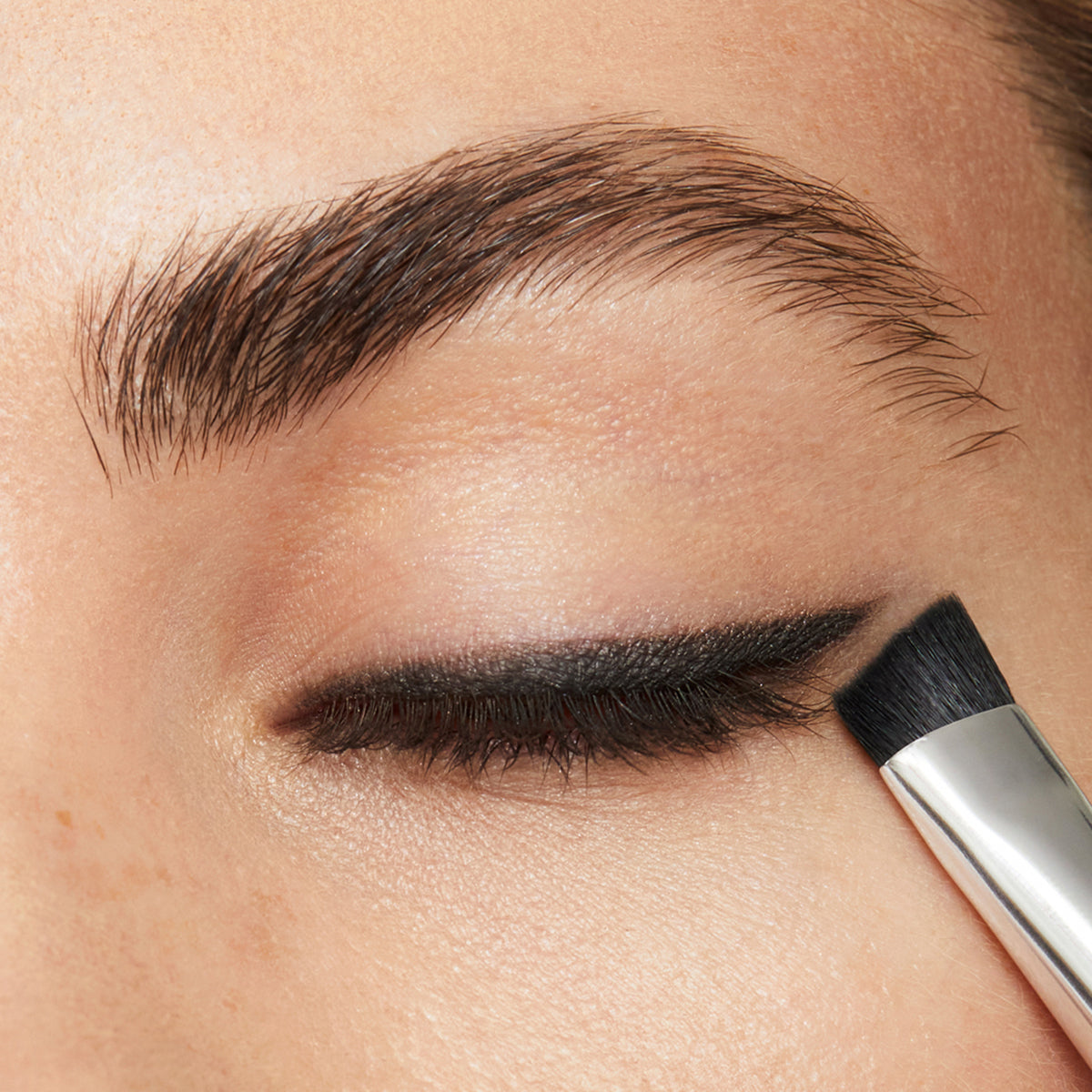 Model applying Licorice eye shadow as a eyeliner