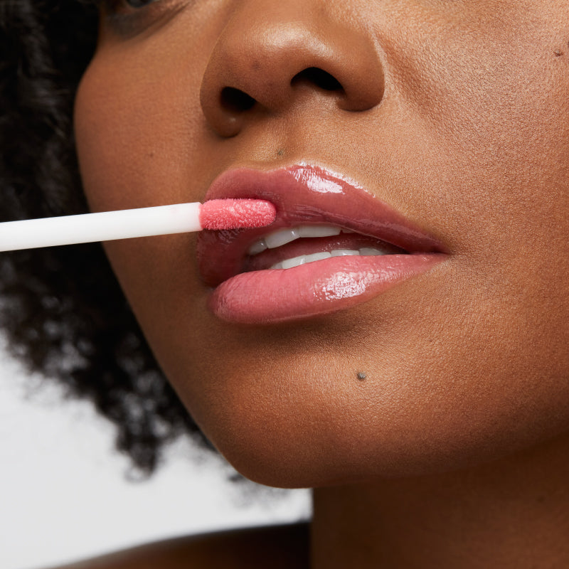 Model applying the pink natural spin on lip gloss on lips